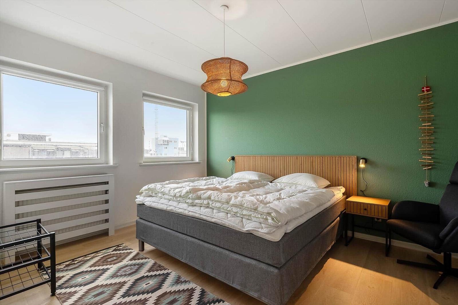 Schlafzimmer mit Bett, grüner Wand und zwei Fenstern.