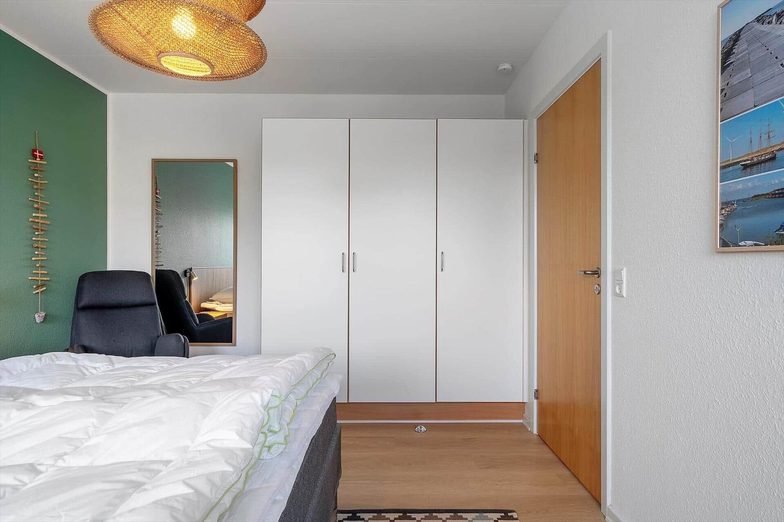 Schlafzimmer mit Bett, Kleiderschrank und Wandspiegel.