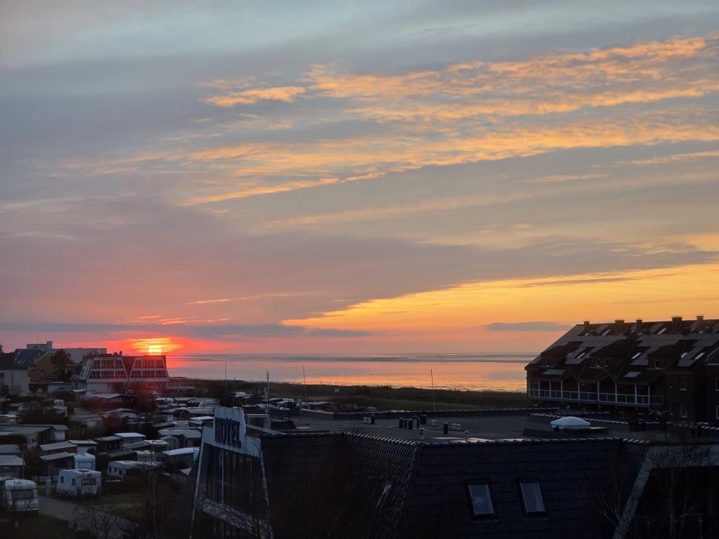 Sonnenuntergang über dem Meer mit Gebäuden und Wohnwagen im Vordergrund.