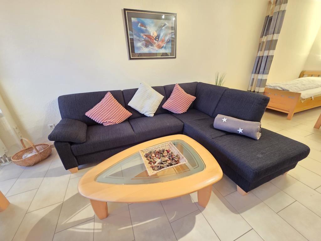 Ein Wohnbereich mit einem dunkelblauen Sofa, einem Holztisch und einem Bett im Hintergrund.