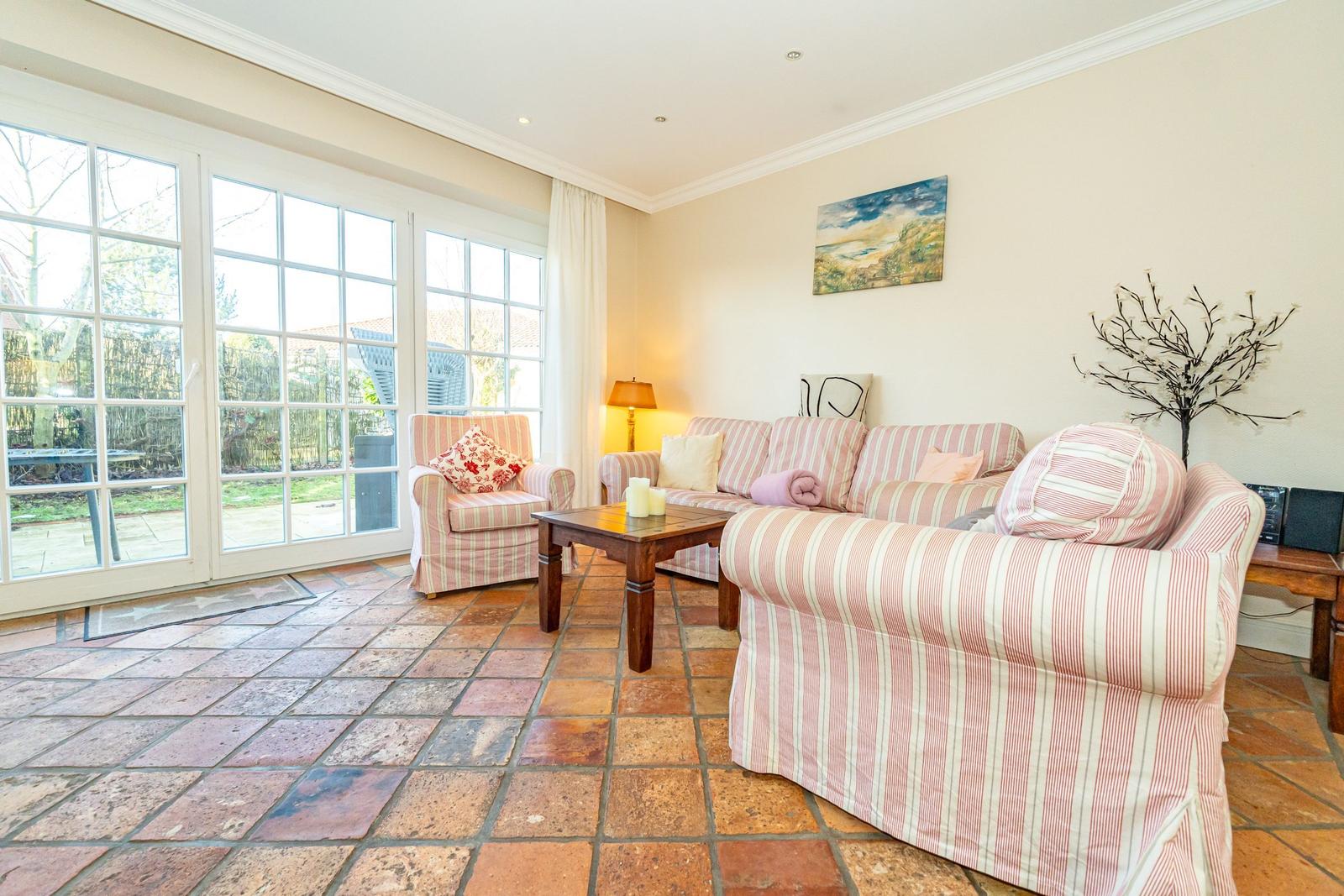 Wohnzimmer mit Sofa, Sessel und Terrassentür. Terrakottboden und Wandbild.