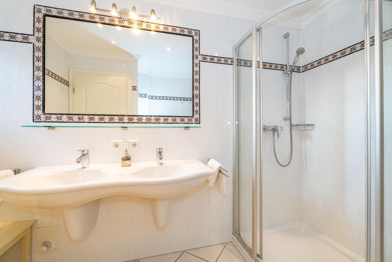 Bad mit Dusche, Waschbecken und Spiegel mit Mosaikrahmen.