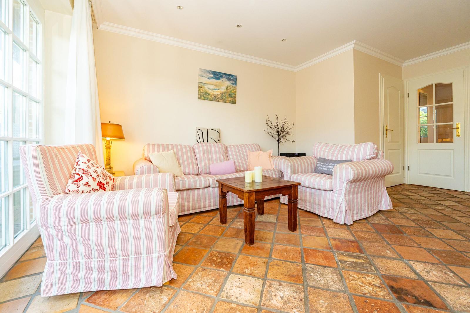 Wohnzimmer mit Streifensofa, Holztisch und Fliesenboden.