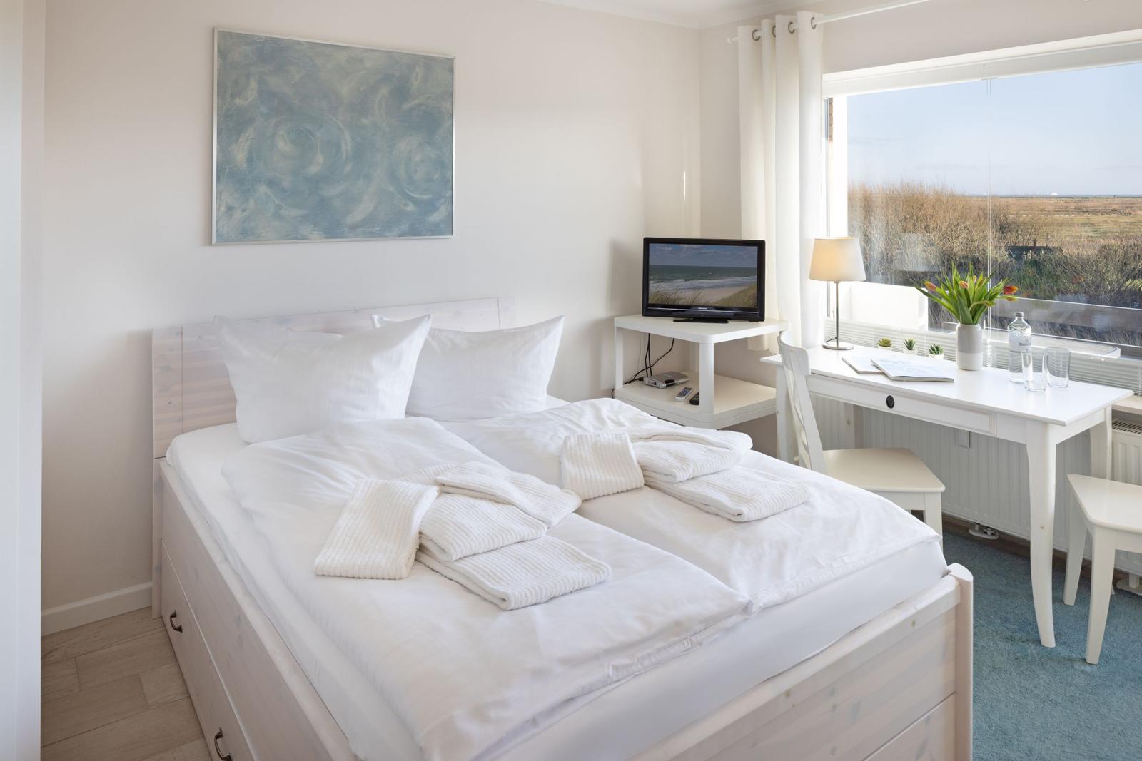 Ein Schlafzimmer mit Doppelbett, Schreibtisch und Fernseher. Durch das Fenster sieht man eine Landschaft.