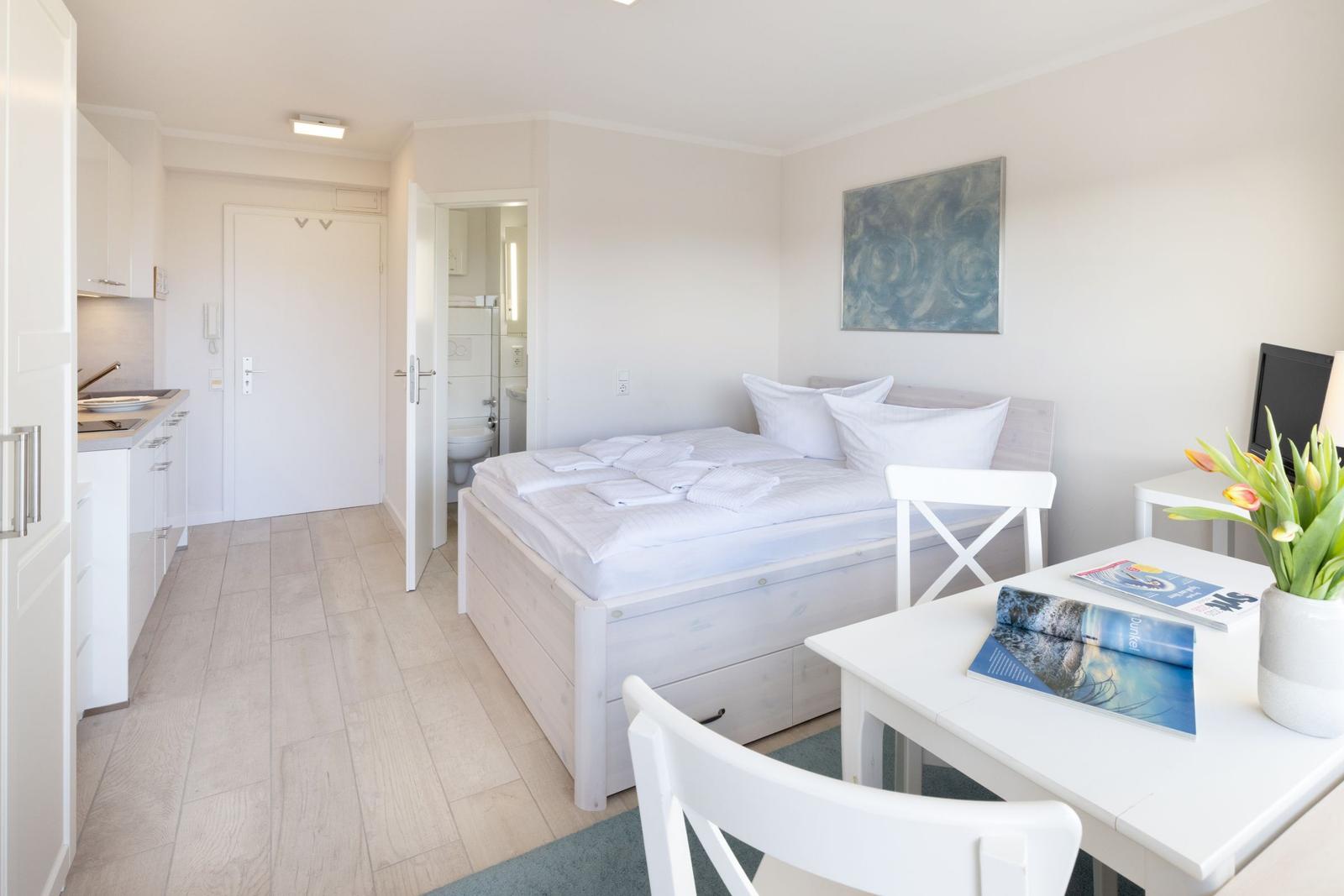 Schlafzimmer mit Bett, Tisch, Stühlen und Küchenbereich. Badezimmer ist angrenzend.