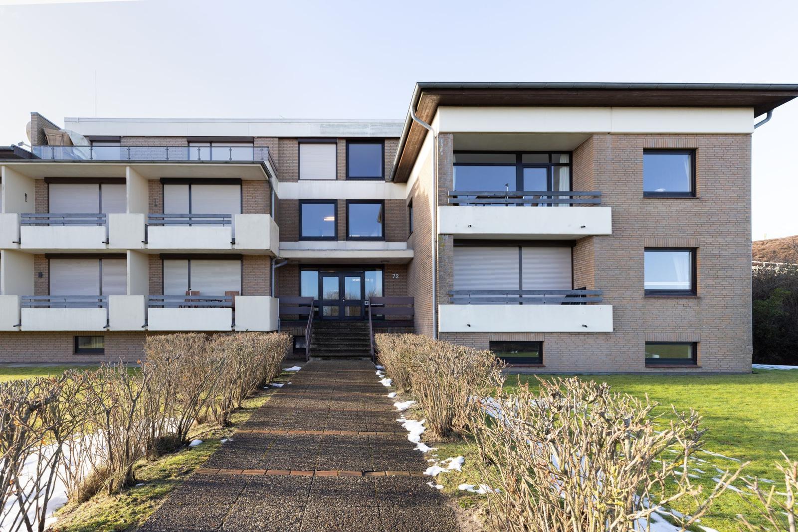 Modernes Mehrfamilienhaus mit Balkonen und Gartenweg.