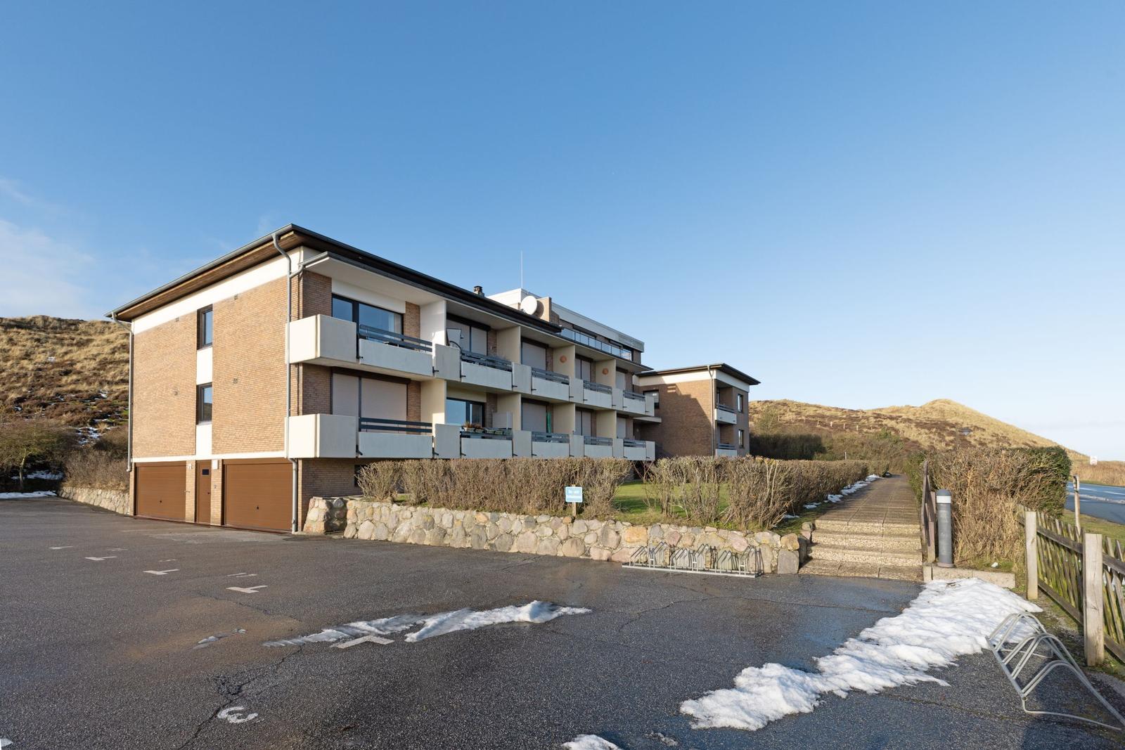 Modernes Mehrfamilienhaus mit Balkonen und Garage. Hinterhof mit Steig und Schneeresten.