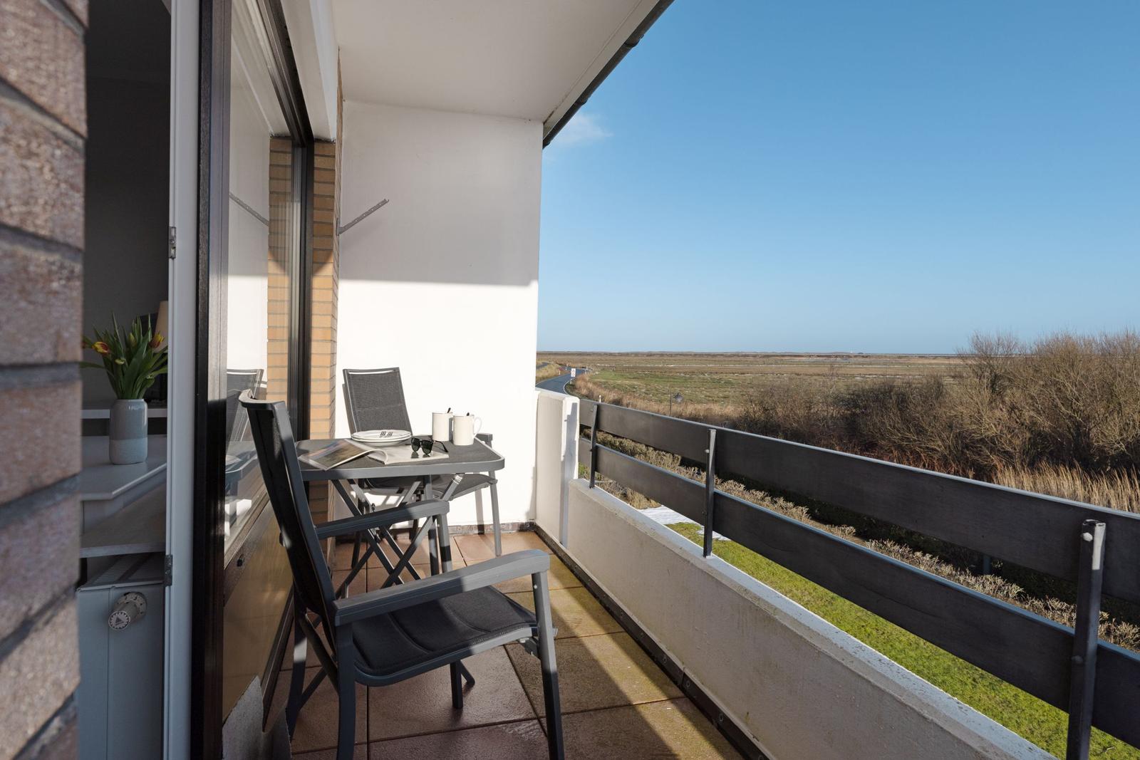 Balkon mit Tisch und Stühlen, Blick auf Felder und Himmel.