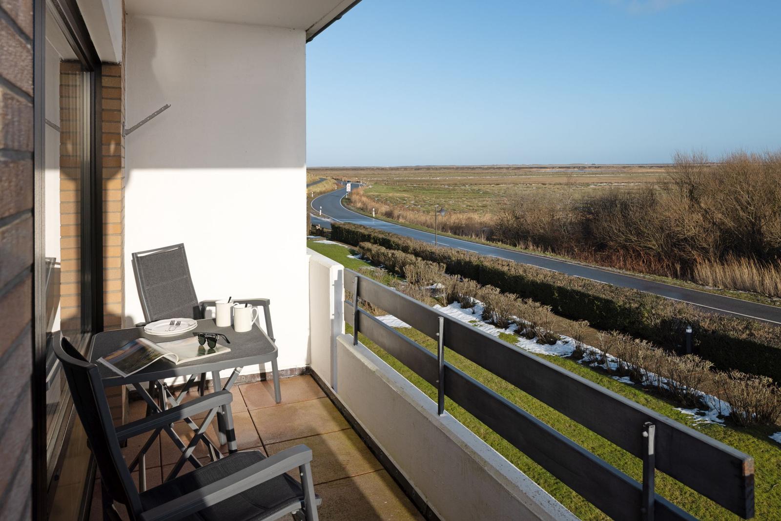 Balcony with table and chairs overlooking a road and open landscape.