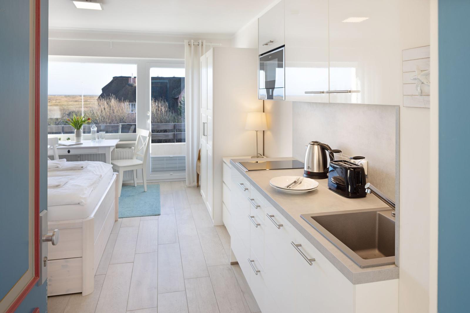 Küche mit Arbeitsplatte, Spüle und Kochfeld. Blick auf Balkon mit Tisch und Stühlen.