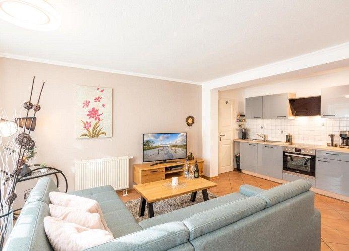 Wohnzimmer mit Sofa, Fernseher und angrenzender Küche mit Arbeitsplatten.