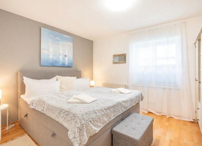 Schlafzimmer mit Bett, Fenster und Wandbild. Holzboden und Vorhänge.
