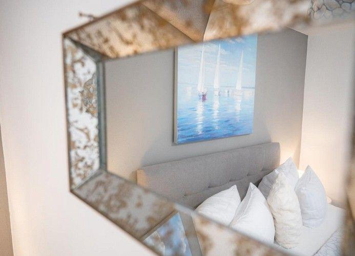 Spiegel zeigt Bett mit Kissen und Wandbild mit Segelbooten.
