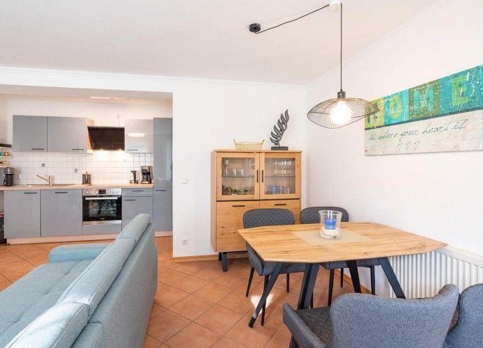 Wohnbereich mit Essbereich, Küche und Wohnzimmer. Holztisch, Sofa und Küchenschränke sichtbar.