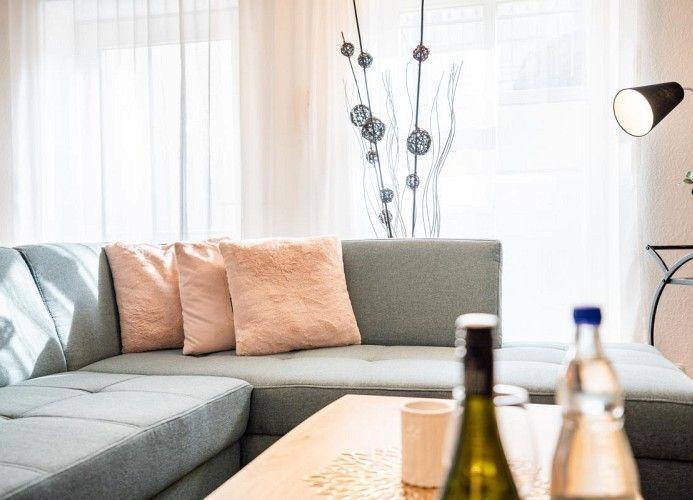 Ein Wohnbereich mit grauem Sofa, rosa Kissen und einem Holztisch mit Flaschen.