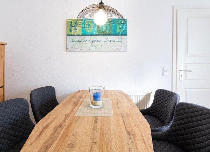Esszimmer mit Holztisch, schwarzen Stühlen und Wandbild. Deckenleuchte über Tisch.