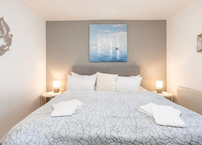 Schlafzimmer mit Doppelbett, Wandbild und Nachttischen mit Lampen.