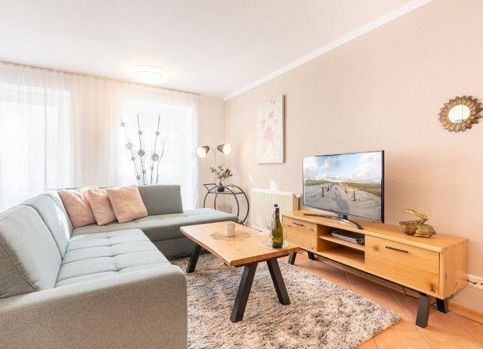 Wohnzimmer mit Sofa, TV und Holztisch. Fenster mit Vorhängen und Wandbild.