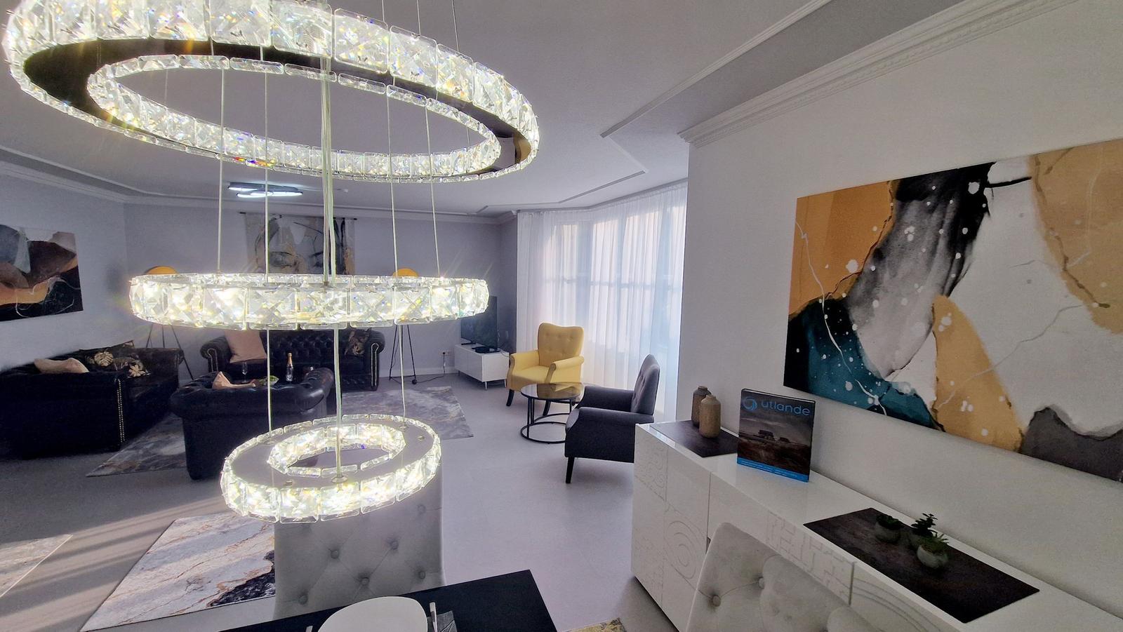 Wohnzimmer mit moderner Deckenleuchte, Sitzgelegenheiten und Wandbildern.