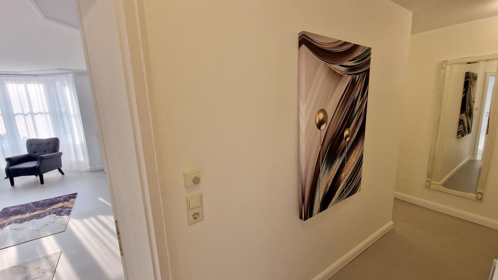Flur mit Wandbild, Spiegel und Sicht auf Wohnbereich mit Sessel und Teppich.