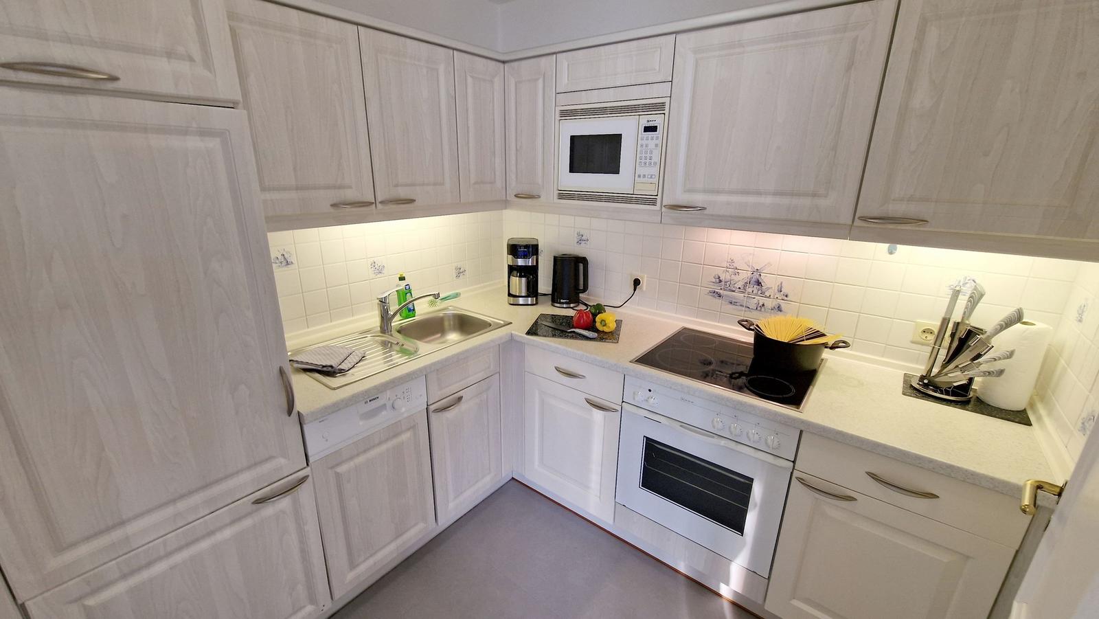 Küche mit weißen Schränken, Spüle, Herd und Mikrowelle.