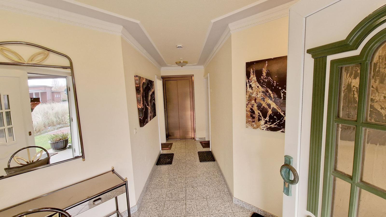 Flur mit Spiegel, Kunstwerken und Tür zum Aufzug.