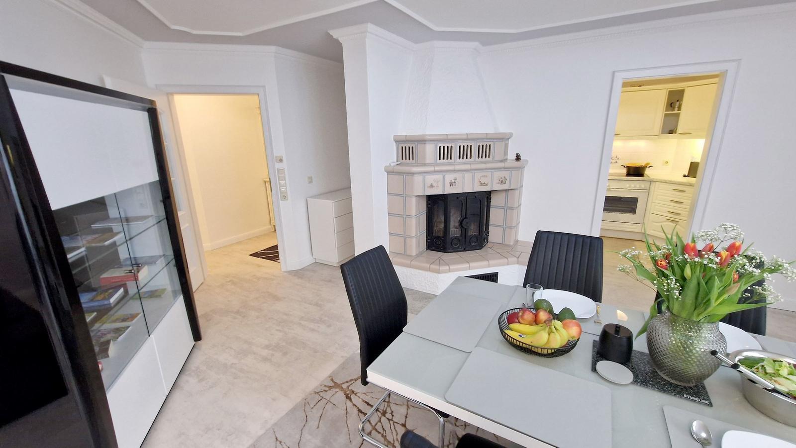 Essbereich mit Tisch, Stühlen und Kamin. Küche und Wohnbereich sind sichtbar.