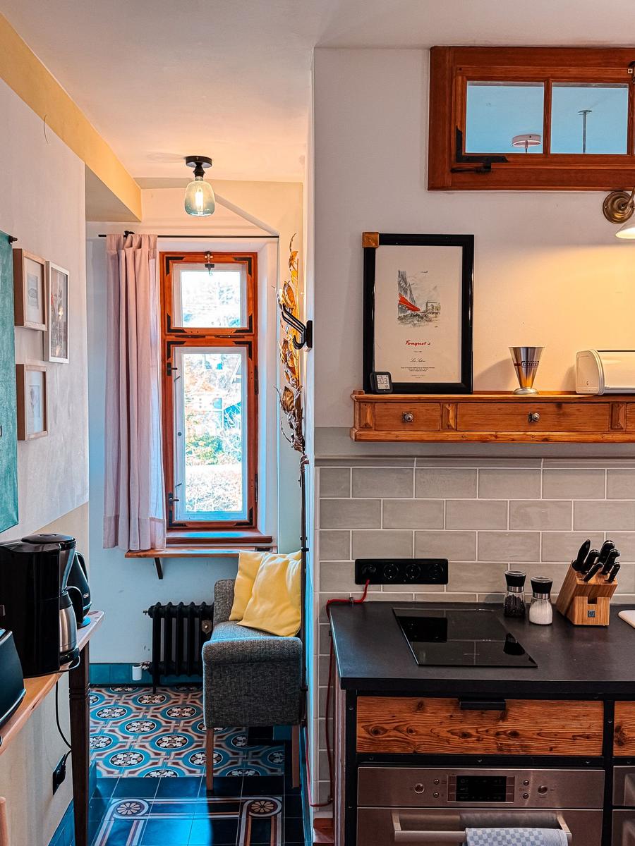 Küche mit Induktionskochfeld und Holzschrank. Nebenraum mit Fenster und gemusterter Fliesenboden.