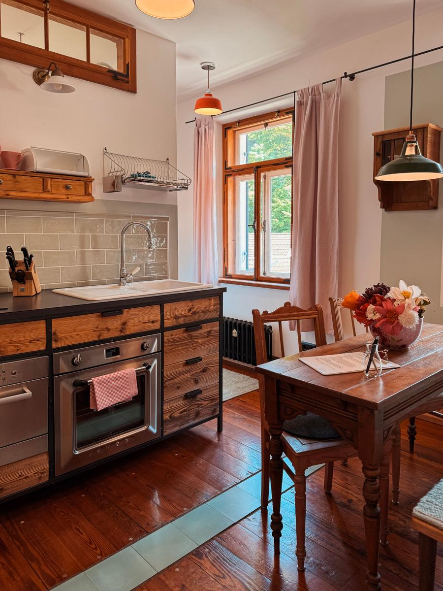 Küche mit Essbereich, Holzmöbel und Fenster mit rosa Vorhängen.