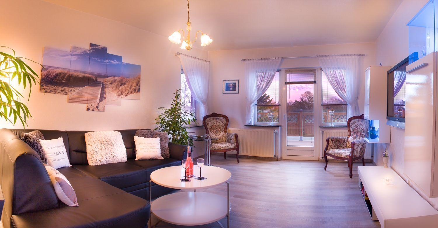 Wohnzimmer mit Sofa, zwei Sessel und Tisch. An der Wand hängt ein Strandbild.