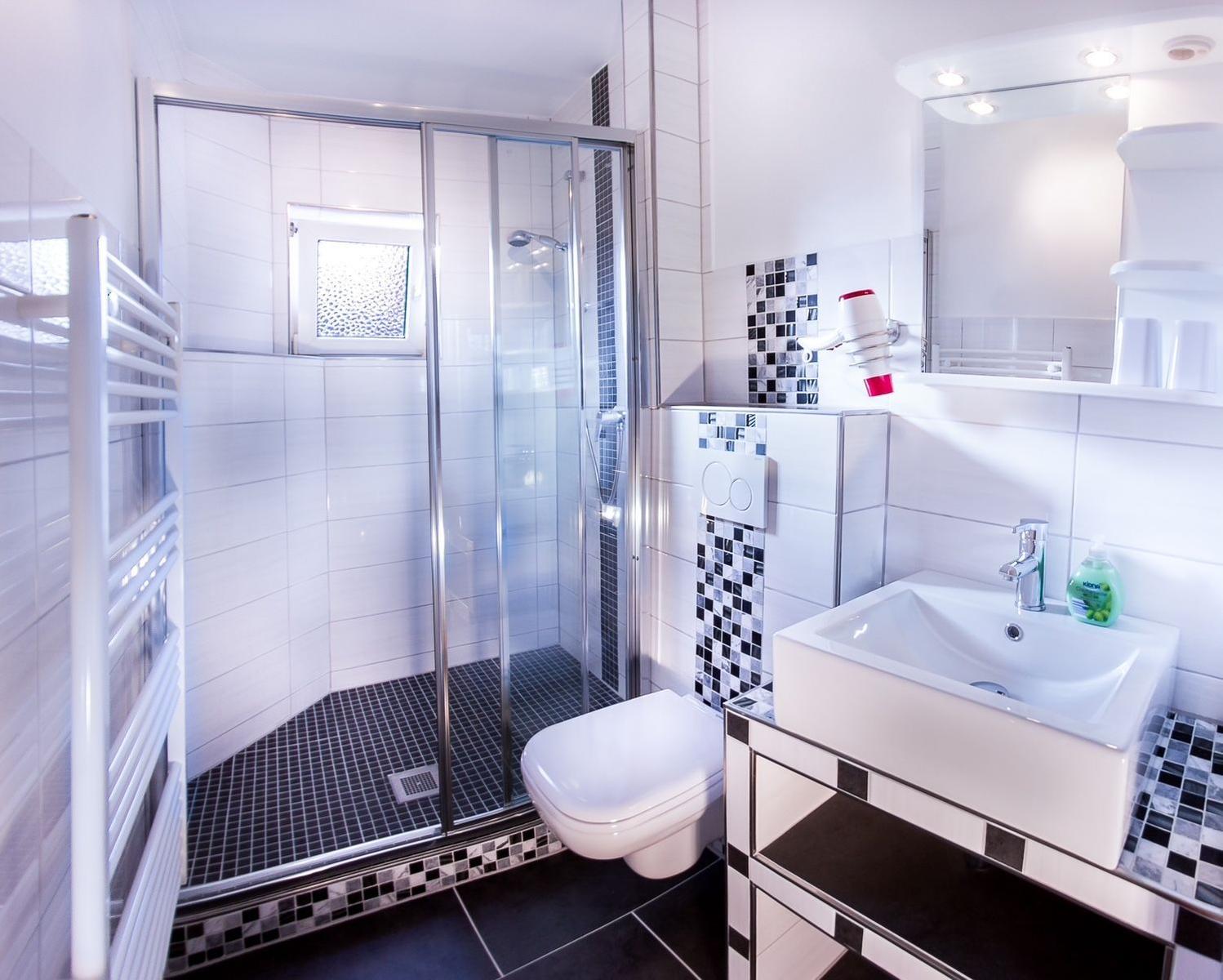 Badezimmer mit Dusche, Waschbecken und Toilette. Fliesen in Weiß und Schwarz.