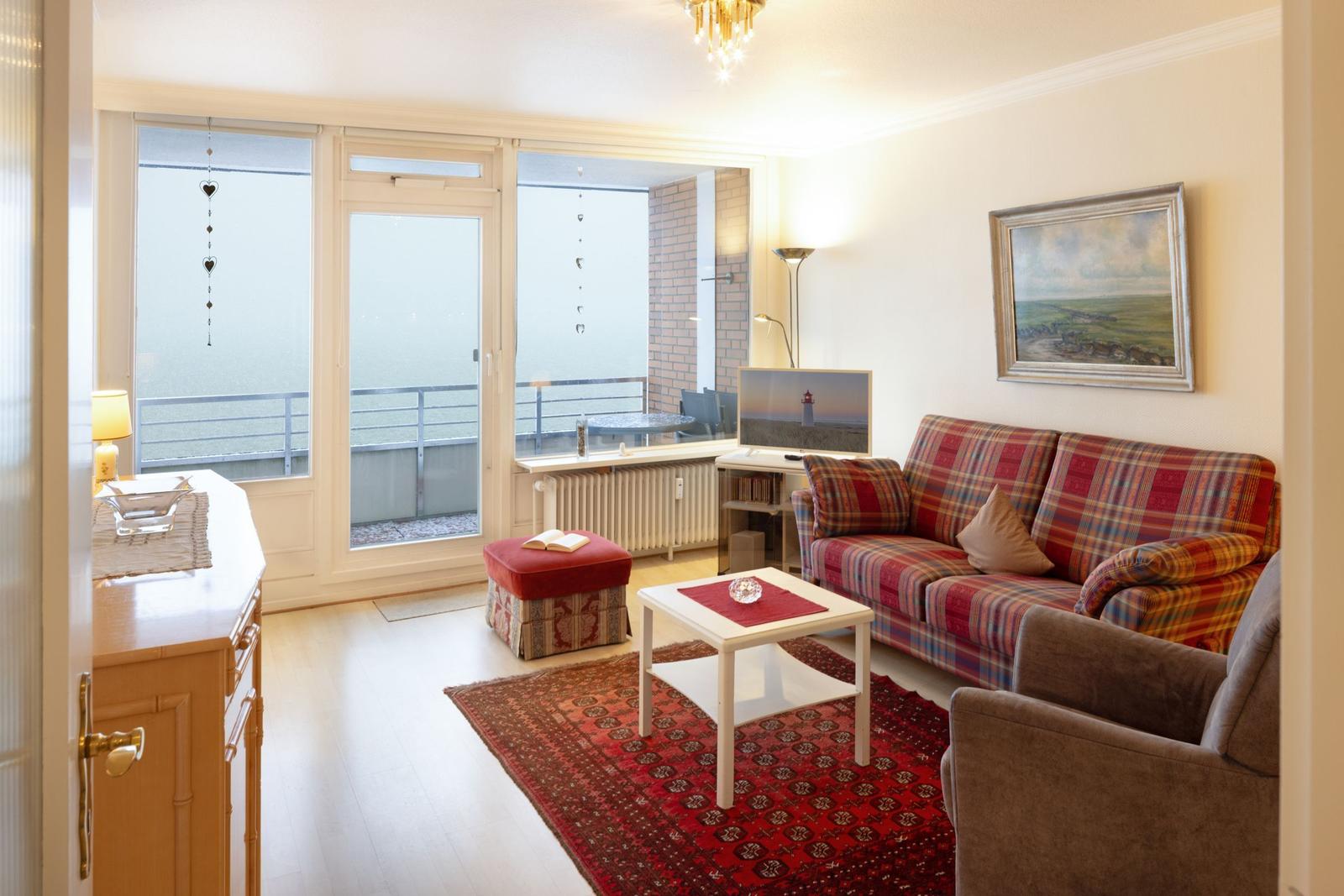 Wohnzimmer mit Sofa, Couchtisch und Balkon. Wandbild und Teppich sind sichtbar.