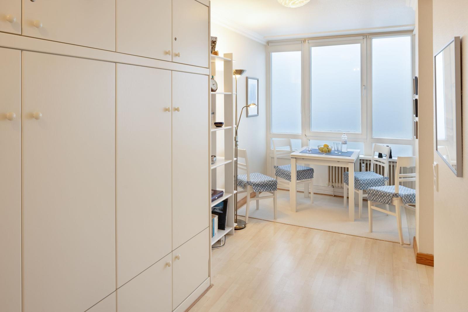 Esszimmer mit Tisch, Stühlen und Fenstern. Nebenher großes Schrankregal.