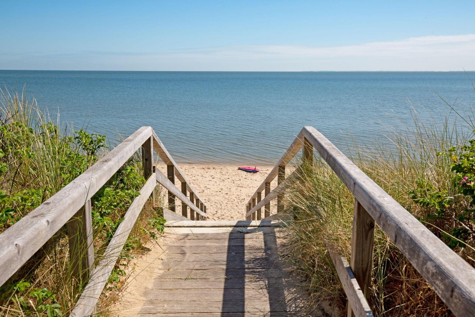 Holzsteg führt zum Strand mit Blick auf das Meer. Ein roter Kajak liegt am Ufer.