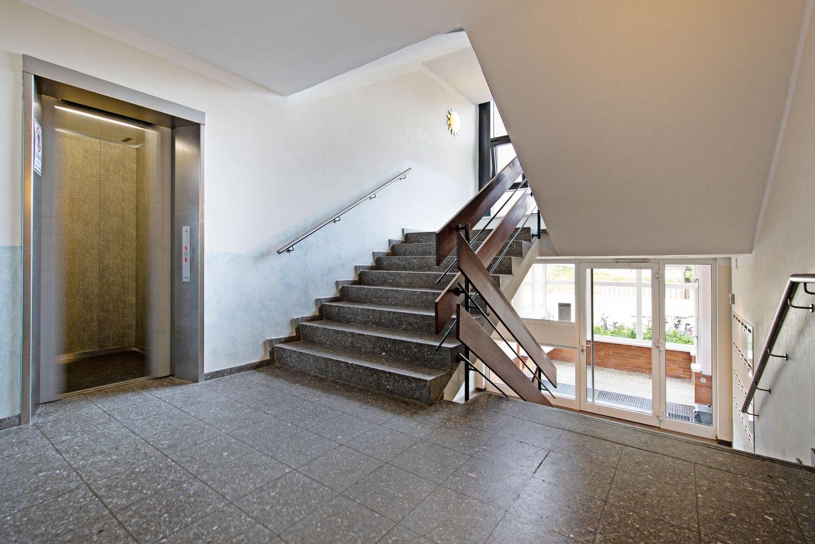 Haus-Eingang mit Aufzug, Treppe und Glastür zum Außenbereich.