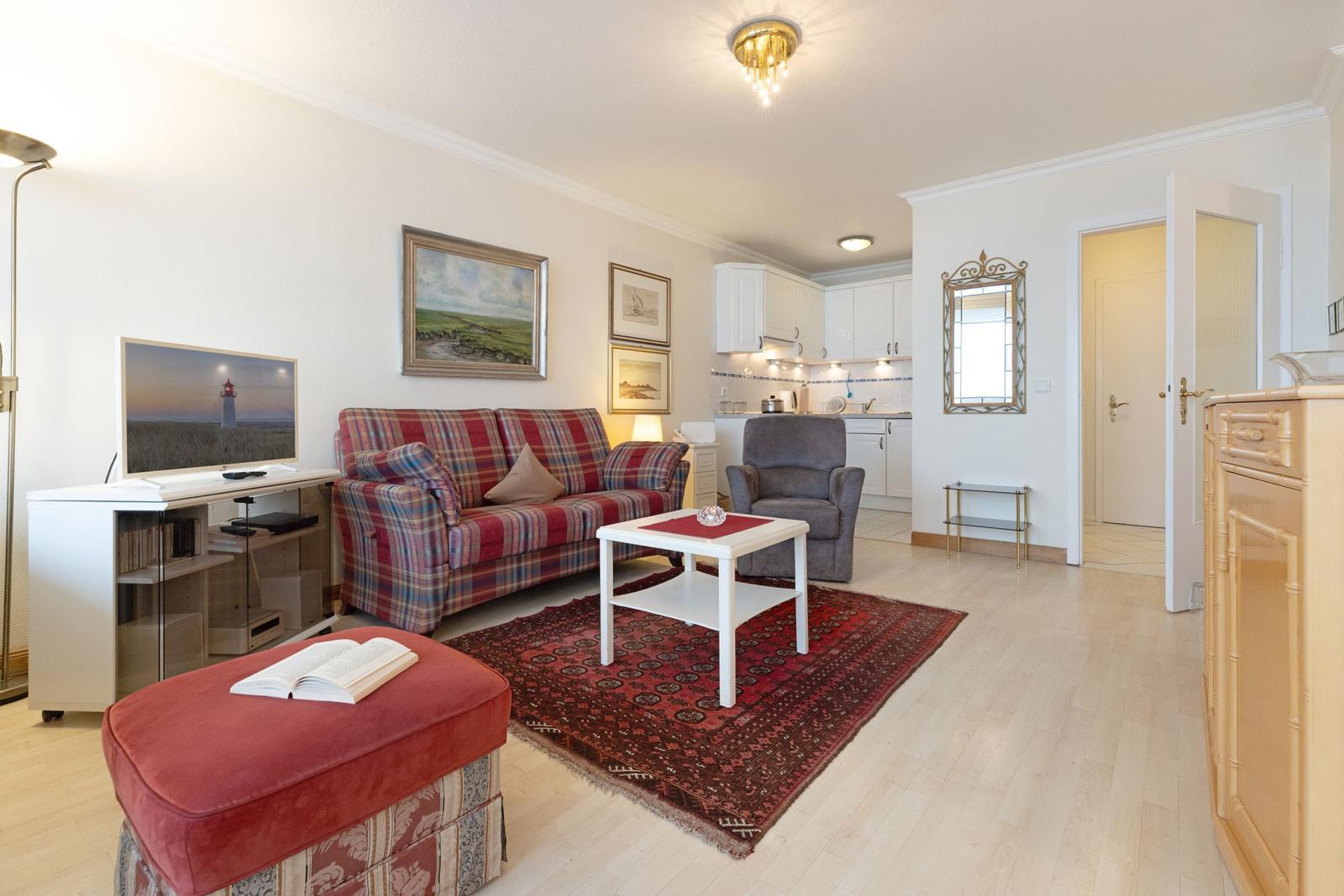 Wohnzimmer mit Sofa, Fernseher und Küchenbereich im Hintergrund.