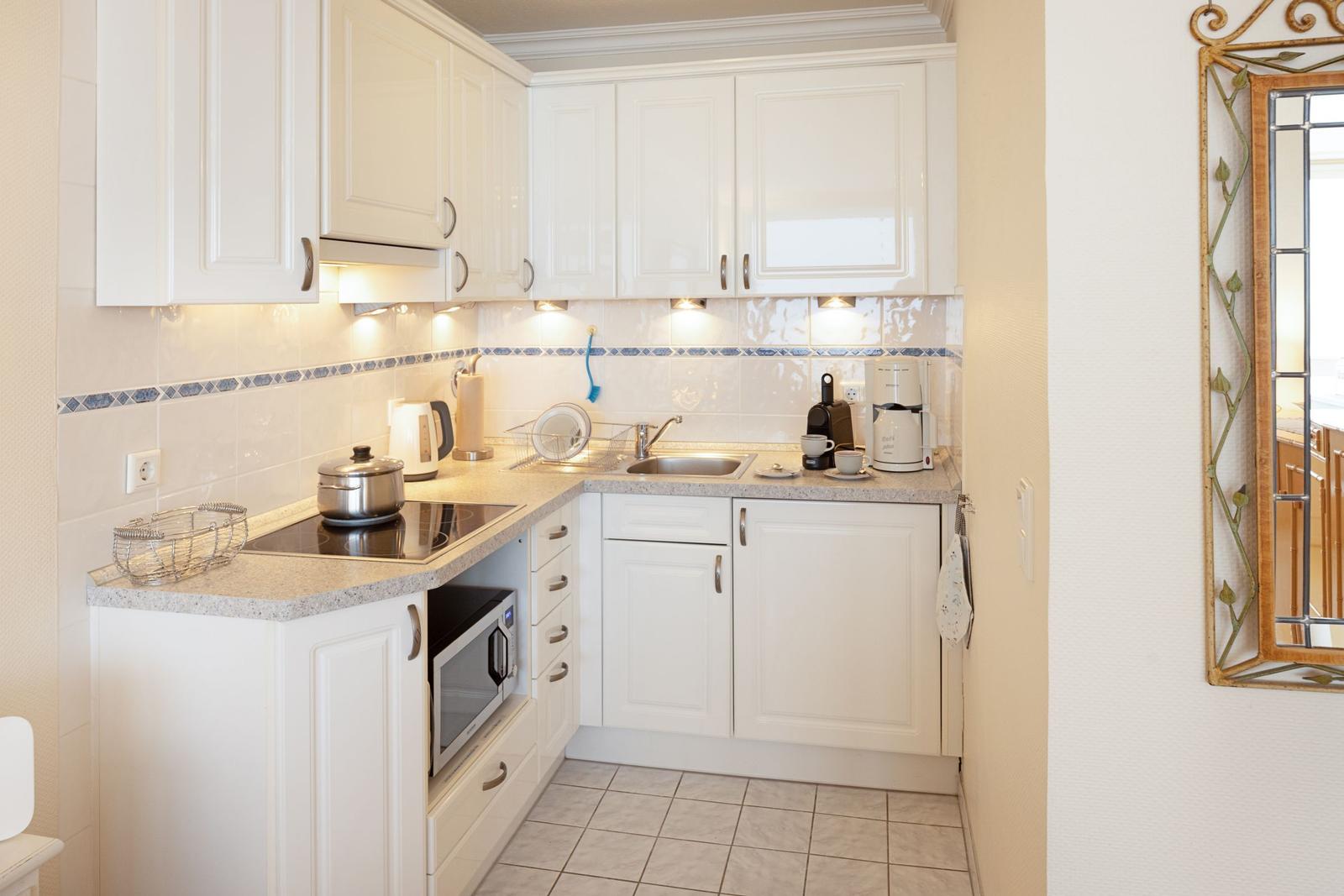 Küche mit weißen Schränken, Arbeitsplatte und Spüle. An der Wand hängt ein Spiegel.