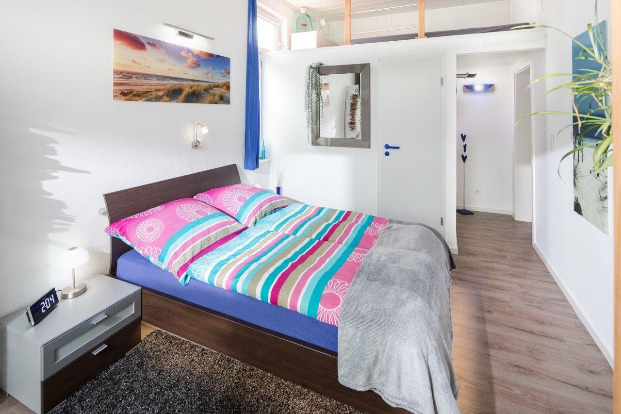Schlafzimmer mit Doppelbett, Nachttisch und Wandbild. Holzboden und Tür zum Flur.