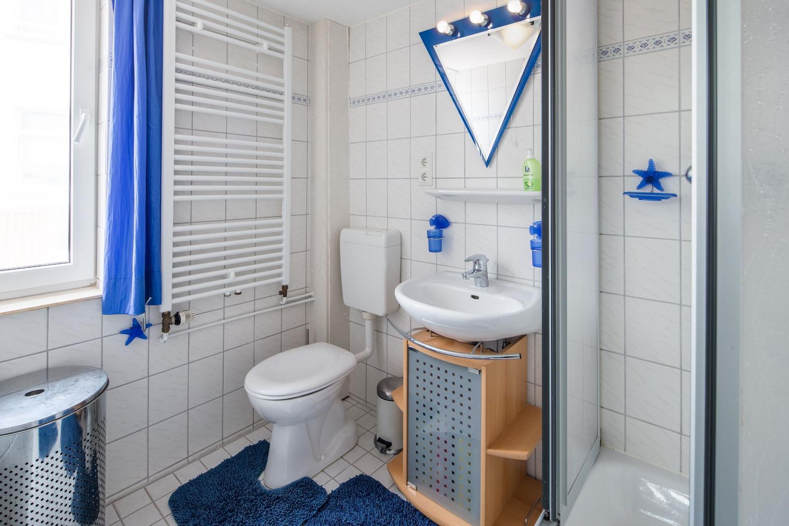 Badezimmer mit Toilette, Waschbecken und Dusche. Blaue Akzente und Fenster.