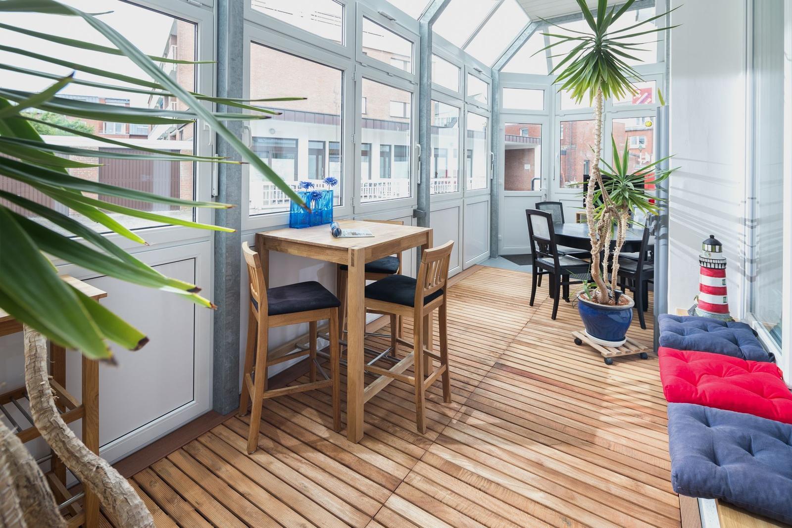 Terrassenbereich mit Holzboden, Tischen, Stühlen und Pflanzen.