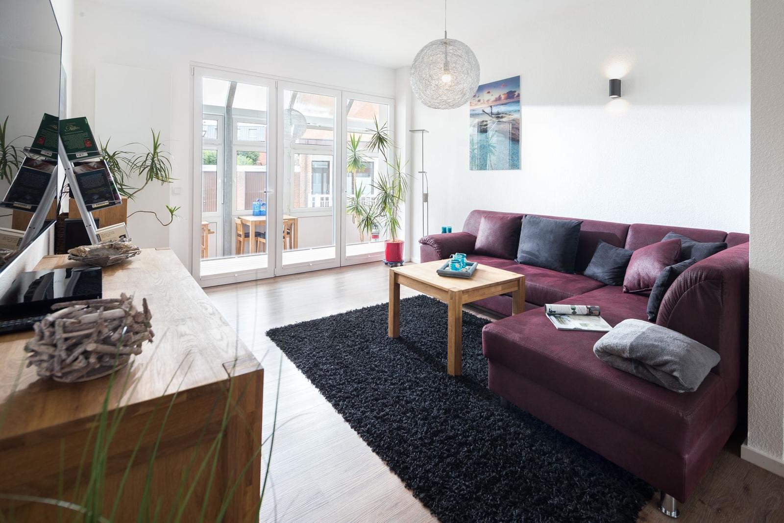 Ein Wohnzimmer mit rotem Sofa, Holztisch und Glasfront zur Terrasse.