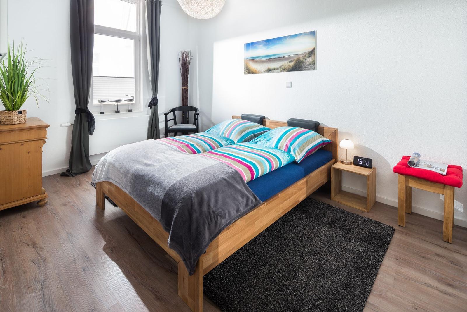 Ein Schlafzimmer mit Holzbett, Fenster, Nachttisch und Bild an der Wand.