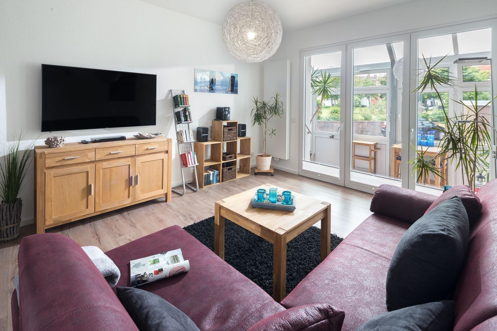 Wohnzimmer mit Sofa, Fernseher und Glastür zur Terrasse.