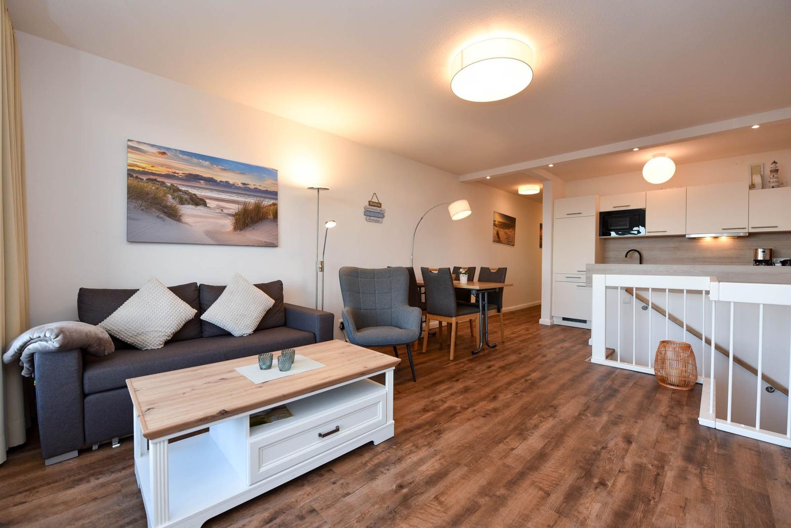 Wohnbereich mit Sofa, Couchtisch und Essbereich. Küche mit Arbeitsplatte und Treppenhaus.