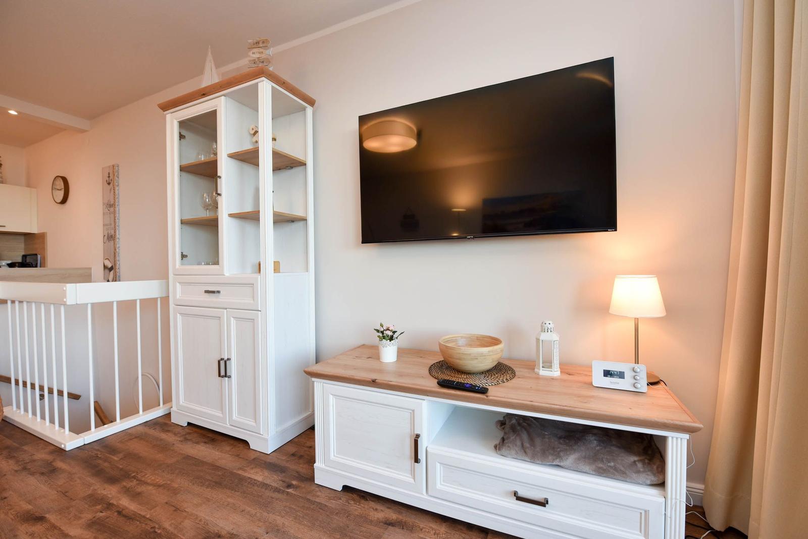 Wohnbereich mit Fernseher, Sideboard und Weinkühler. Holzboden und warme Beleuchtung.