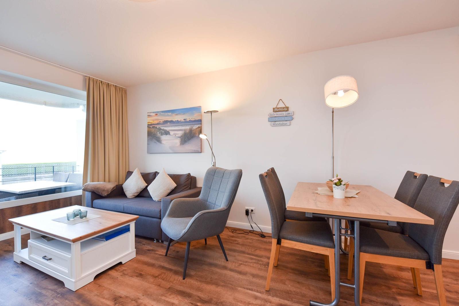 Wohn- und Essbereich mit Sofa, Stuhl, Tisch und Fenster zur Terrasse.