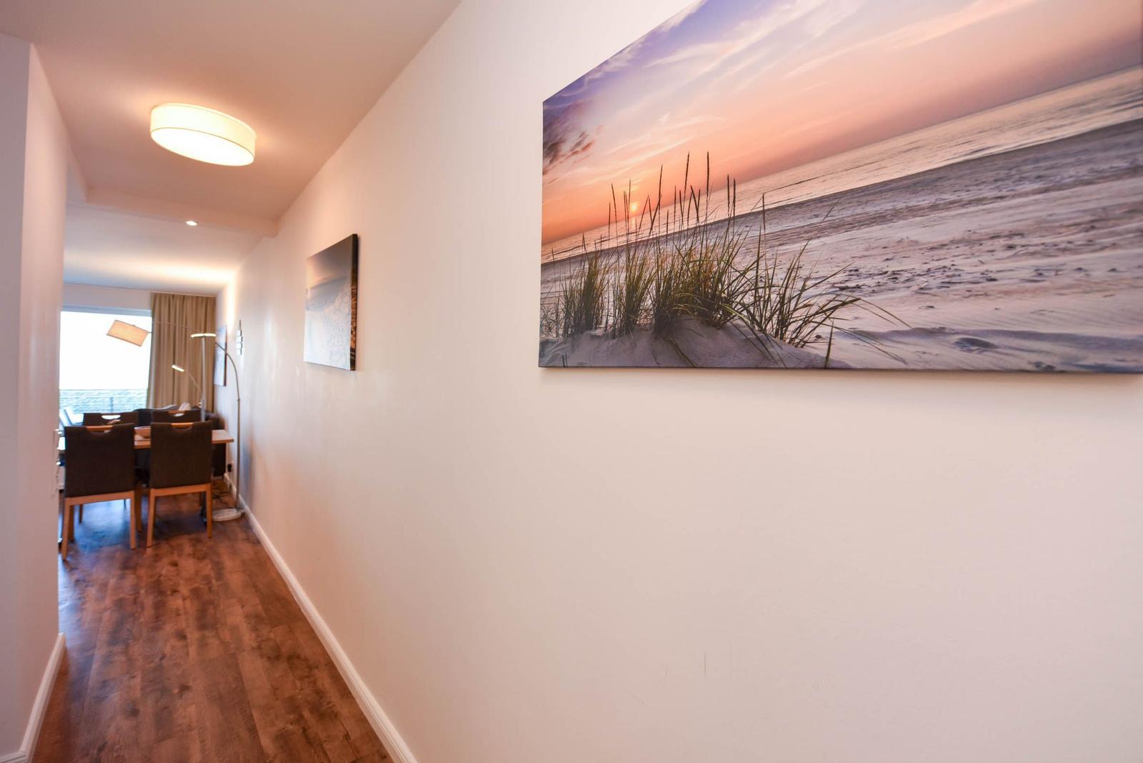 Flur mit Holzboden und Wandbildern, Sicht in Essbereich mit Tisch und Stühlen.
