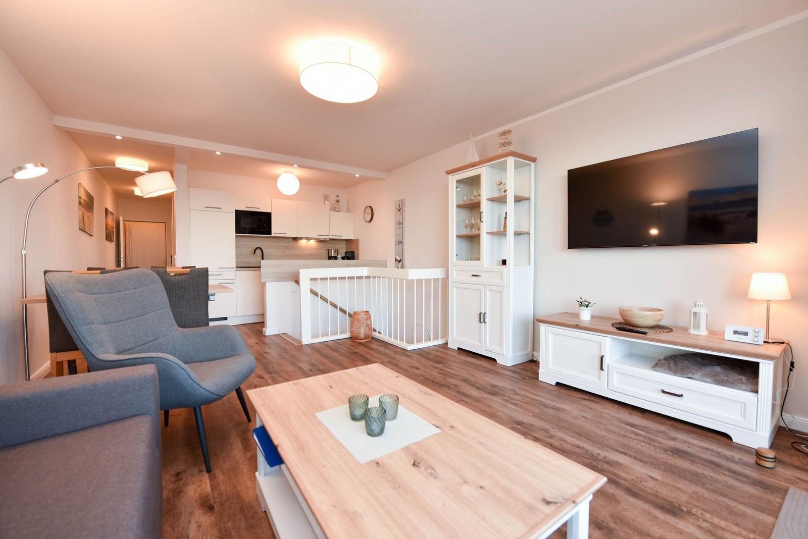 Wohnzimmer mit Fernseher, Esstisch und Küche im Hintergrund.