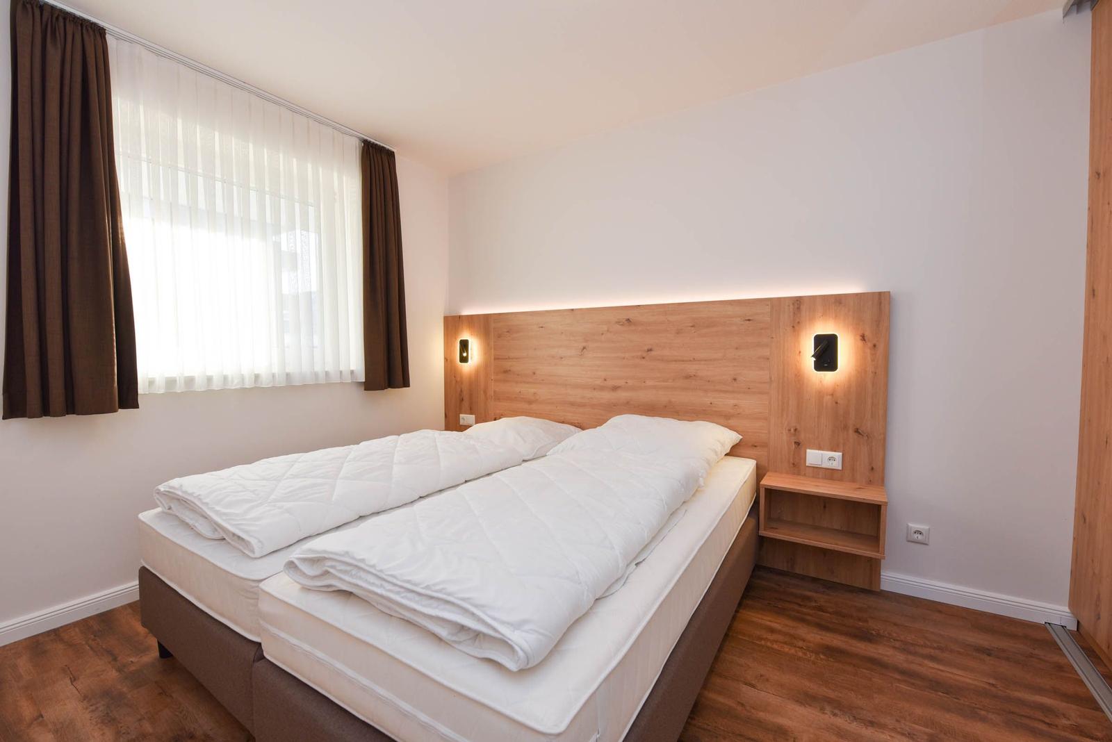 Schlafzimmer mit Doppelbett, Holzfußboden und Fenster mit Jalousie.