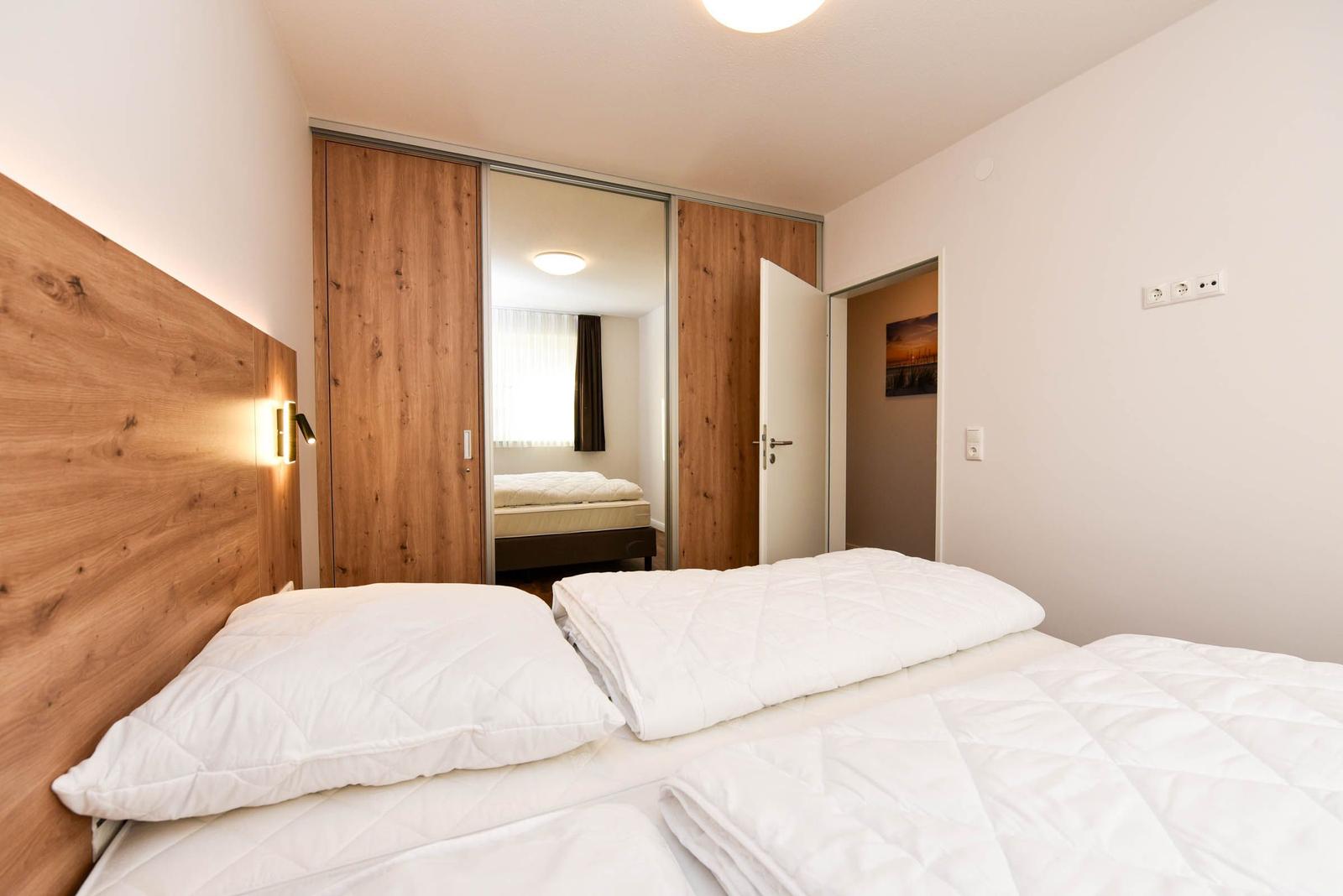 Schlafzimmer mit Doppelbett, Holzschrank und Nachttischbeleuchtung.